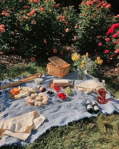 a picnic blanket with food on it in the grass next to some flowers and bushes