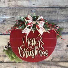 a merry christmas sign hanging on the side of a wooden wall with holly and pine cones