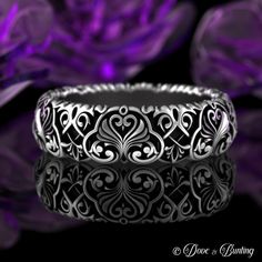 an ornate wedding band with filigrees and scrolls on the side, sitting in front of purple flowers