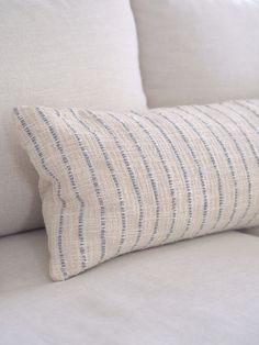 a close up of a pillow on a couch with white linens and blue stripes