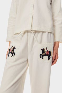 Relaxed pants in airy off-white cotton canvas with a drawstring waist. The straight cut design introduces an elevated take on a classic – with delicate broderie anglaise trims and an embroidered horse motif at the front pockets. Style with the Kotyk Embroidered Cotton Shirt for a truly unique ensemble, featuring artwork by pattern designer Yuliya Geras'ko. Embroidered Cotton Loungewear Pants, Embroidered Cotton Pants For Loungewear, White Cotton Bottoms With Embroidered Hem, Casual Cotton Bottoms With Broderie Anglaise, Embroidered Cotton Bottoms For Daywear, Off White Cotton Pants With Elastic Waistband, White Straight Pants With Chikankari Embroidery, White Chikankari Embroidered Straight Pants, Spring White Pants With Chikankari Embroidery