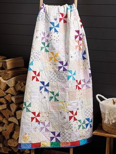 a quilt hanging on a clothes rack next to stacked logs and a basket full of firewood