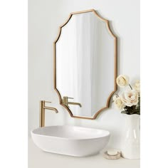 a white sink sitting under a mirror next to a vase with flowers