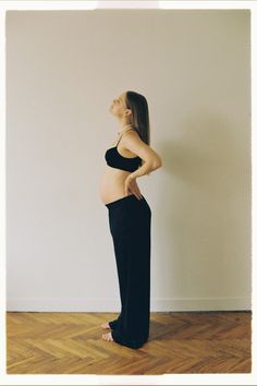 a pregnant woman standing in front of a white wall with her hands on her hips