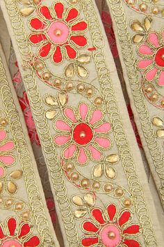 red and pink flowers on beige fabric with gold trimmings, close up view