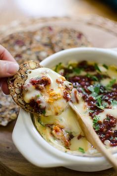 a person dipping cheese into a bowl of soup with a wooden spoon on the side