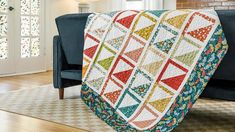 a couch with a colorful quilt on it in front of a brick wall and windows