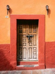 an open door on the side of a red and orange building with two light fixtures