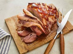 sliced meat sitting on top of a cutting board next to a knife and fork,