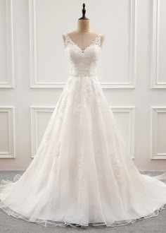 a wedding dress on display in front of a white wall with a mannequin