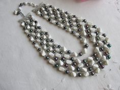 The 5-strand necklace has irregular shaped white beads separated by round dark iridescent beads.  The beads in the center are larger than the beads toward the hook closure. The longest strand measures 17 inches and the other strands are incrementally shorter: 15 1/2 inches, 14 1/2inches, 13 1/2inches and 11 inches.  There is a 3 inch extender with a hook closure and a silver tone clasp which is marked "Japan".  This makes the necklace up to 3 inches longer. Dazzling and elegant! White Multi-strand Pearl Necklace, Multi-strand Pearl Beaded Necklace With Faceted Beads, White Beaded Multi-strand Pearl Necklace, White Multi-strand Pearl Beaded Necklaces, White Multi-strand Beaded Pearl Necklace, Pearl White Multi-strand Beaded Necklace, White Mother Of Pearl Necklace With Gemstone Beads, White Double Strand Beaded Necklace With Colorful Beads, White Double Strand Faceted Beads Necklace