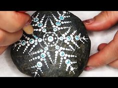 someone is painting a rock with white and blue dots