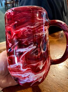 a red and white coffee mug sitting on top of a wooden table next to a person