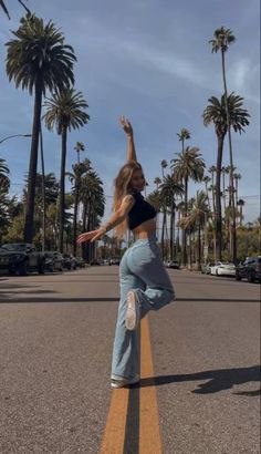 a woman is standing on one leg in the middle of an empty street with palm trees behind her