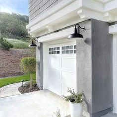 a white garage with two lights on the side of it and a potted plant in front