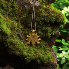 a gold necklace with an ornate design hanging from a mossy tree branch in the woods