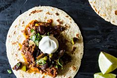 two tortillas topped with meat and sour cream on top of a black surface