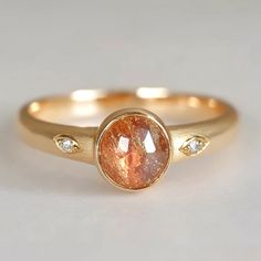 a gold ring with an orange stone and two white diamonds on the bottom, set in yellow gold