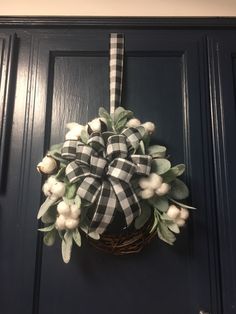 a wreath hanging on the front door with white flowers and greenery attached to it