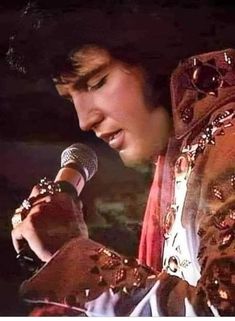 elvis presley singing into a microphone with his hand on his hip and wearing gold bracelets