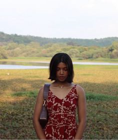 a woman in a red and white dress standing next to a body of water with trees in the background