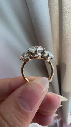 a person holding a three stone ring in their left hand, with the diamond set on it's middle finger