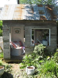 a small house with a metal roof in the middle of some bushes and trees,