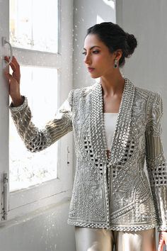 A slate coloured tissue jacket with folded lapels is rendered with intricate cutwork and thread and embroidery. Paired with ivory choli and slate-coloured charmeuse box trousers with embroidered hems; this outfit exudes sheer elegance. Model Height is 5'6 jacket length is 26" Elegant Silk Sherwani With Resham Embroidery, Elegant Embroidered Silk Sherwani, Elegant Sets With Pearl Embroidery And Traditional Drape, Elegant Sets With Pearl Embroidery For Reception, Elegant Set With Pearl Embroidery For Reception, Elegant Silk Sherwani With Traditional Drape, Silk Bandhgala With Intricate Embroidery For Wedding, Elegant Embellished Front Open Sets, Elegant Festive Sets With Lace Work