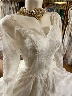 a white wedding dress on display in a store with lots of dresses hanging up behind the mannequin