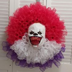 a creepy clown mask hanging on a door with red and white ruffles around it