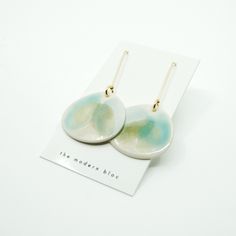 two white and green earrings with gold earwires sitting on top of a card