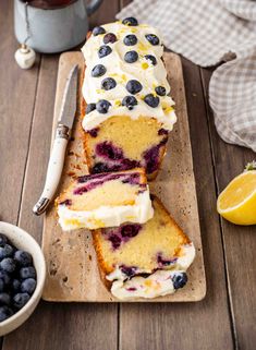 a loaf of lemon blueberry pound cake on a cutting board next to a bowl of blueberries