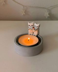 two white cats sitting on top of a table next to a lit candle