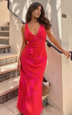 a woman in a long red dress is standing on the stairs with her hand out