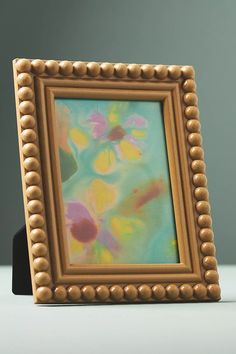 an ornate wooden frame with beaded edges holds a painting in the center and sits on a white surface