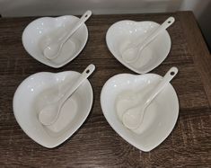 four white heart shaped bowls with spoons in them sitting on a table next to each other