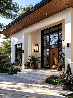 the front entrance to a house with potted plants on the steps and large windows