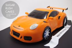 an orange sports car cake on a black table with white ribbon around it and the words sugar rush cakes written in spanish