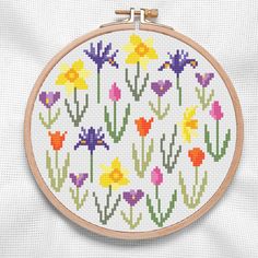 a cross stitch pattern with colorful flowers on it's hoop hanging from a wall