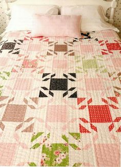 a bed with a pink and green quilt on it's headboard next to a pillow