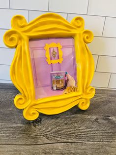 a yellow frame with a cake in it on top of a wooden table next to a white brick wall