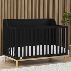 a black crib sitting on top of a wooden floor next to a potted plant