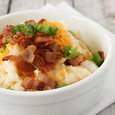 a white bowl filled with mashed potatoes topped with bacon and green onions