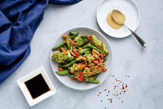 a white plate topped with broccoli and peppers next to a bowl of sauce