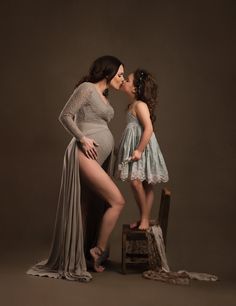 a pregnant woman kissing her daughter's cheek while standing next to a wooden chair