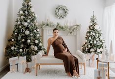 a woman in a brown dress sitting on a white couch next to christmas trees and presents