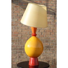 a yellow lamp sitting on top of a table next to a brick wall with a white shade