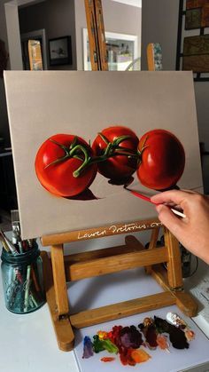 a person is painting three tomatoes on an easel