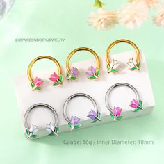 four pairs of flower shaped nose rings on a white display stand with flowers in the background