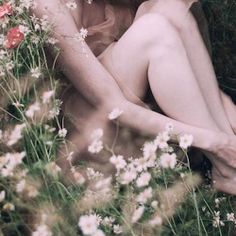 a nude woman sitting in the grass with flowers around her neck and hands behind her head